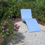 A whimsical blue bench in a private space comfortably curves for lying down amidst the flora.